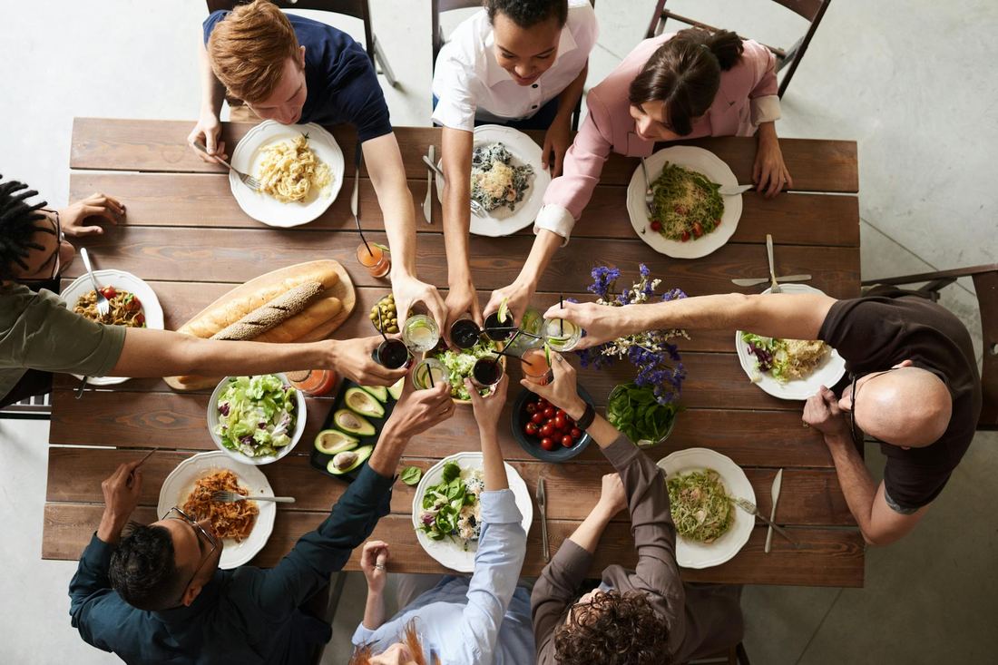 A long table seen from above — many pairs of hands meeting in the middle over a shared meal